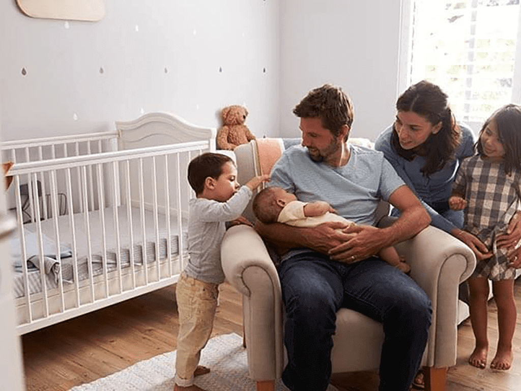 small family gathered around dad holding new born child in nursery